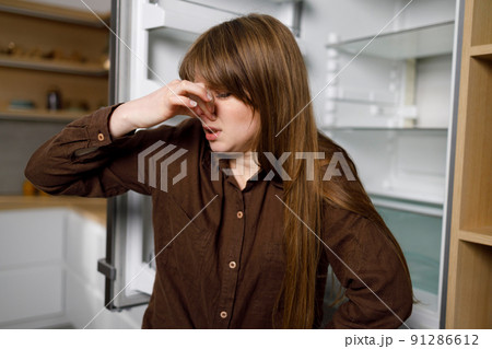 Young woman close her nose because of the nasty smell coming from the refrigerator 91286612