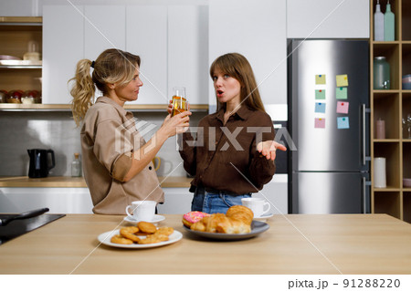 Teen daughter pours her heart out to her mom in the kitchen. Two women drinking juice. 91288220