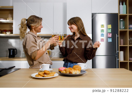 Mom and daughter talk about personal things drink juice and eat sweets in the kitchen 91288222