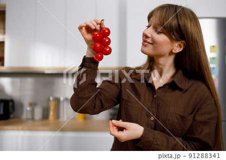Pretty young woman looking at cherry tomatoes on branch on the home kitchen 91288341