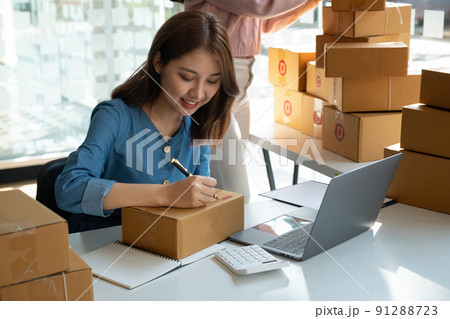 Asian business woman on sofa using a laptop computer checking customer order online shipping boxes at home. Starting SME Small business entrepreneur freelance. Online business, SME Work home concept Asian business woman on sofa using a laptop computer checking customer order online shipping boxes at home. Starting SME Small business entrepreneur freelance. Online business, SME Work home concept 91288723