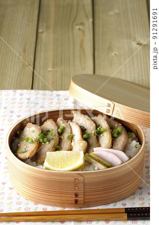 曲げわっぱに漬物とカットレモンと豚トロが入っている焼肉弁当 91291691