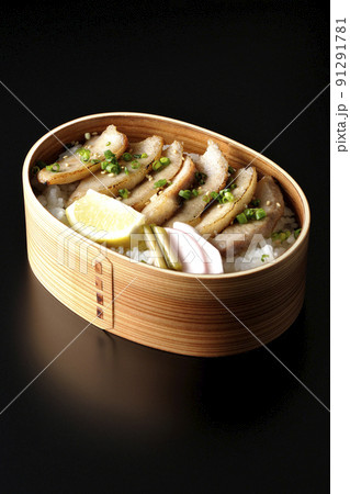 曲げわっぱに漬物とカットレモンと豚トロが入っている焼肉弁当を黒背景で撮影 91291781