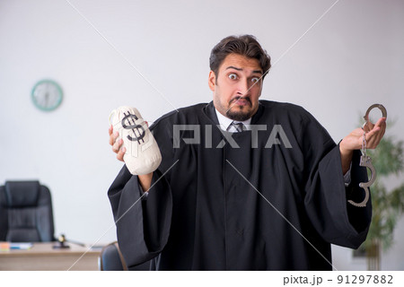 Young male judge holding moneybag in corruption concept Young male judge holding moneybag in corruption concept 91297882