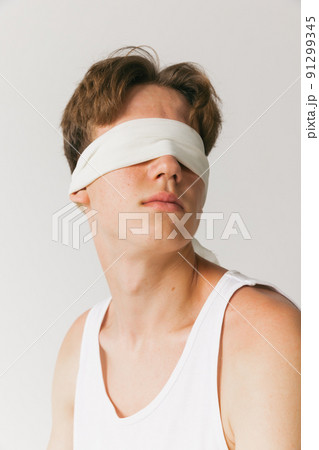 Portrait of young man with blindfold sitting on chair isolated on white studio background. Concept of fashion, youth, emotions, facial expression, ad 91299345