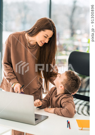 Mother smiles to her son who is sitting at laptop 91300896