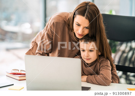 Loving mom helps son with homework while sitting at laptop. Woman with a little boy at computer. Home schooling Loving mom helps son with homework while sitting at laptop. Woman with a little boy at computer. Home schooling 91300897