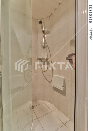 Flush toilet located between sink and shower in small tiled bathroom of contemporary apartment 91301351