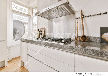 Modern minimalist style interior design of studio apartment with open white kitchen and dining zone with table and chairs illuminated by loft style lamp Modern minimalist style interior design of studio apartment with open white kitchen and dining zone with table and chairs illuminated by loft style lamp 91302258