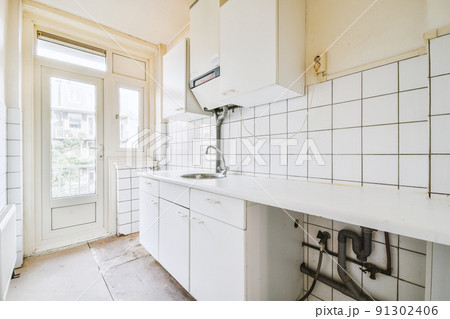 Fragment of interior of light narrow home kitchen with minimalist style white furniture with sink and stove 91302406