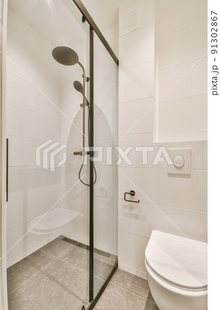 Shower faucets attached to tiled wall near glass partition and ornamental curtail in washroom at home 91302867