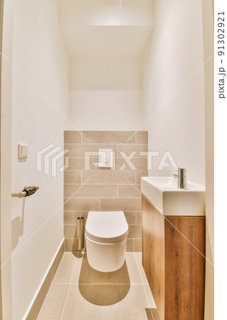 Modern flush toilet and ceramic sink installed on white tiled walls near mirror and towel in small restroom at home 91302921