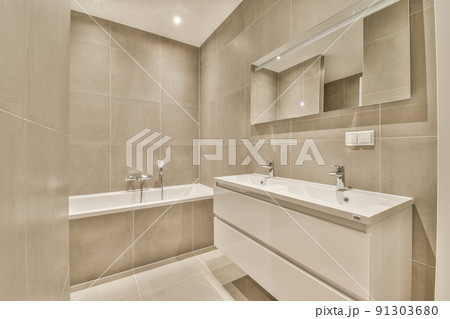Sink with tap and liquid soap hanging on tiled wall under mirror in contemporary restroom at home 91303680