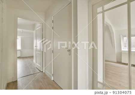 Narrow corridor with white walls and doors leading to spacious room with windows and parquet floor in modern apartment Narrow corridor with white walls and doors leading to spacious room with windows and parquet floor in modern apartment 91304075