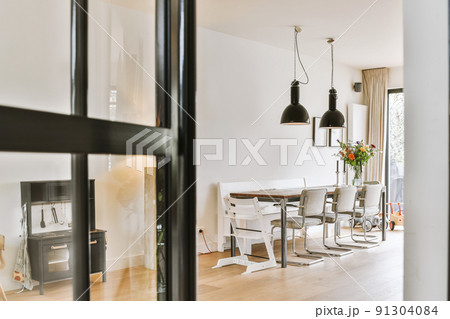 Comfortable chairs and wooden table with flowers placed under stylish lamps against wall Comfortable chairs and wooden table with flowers placed under stylish lamps against wall 91304084