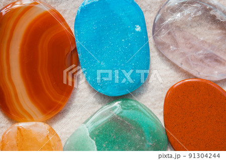 Background of semi-precious multicolored polished stones, pebbles on light white sand on a seashore beach. Stones macro shot. Mineral rocks backdrop wallpaper. Precious jasper stone. Geology concept. Background of semi-precious multicolored polished stones, pebbles on light white sand on a seashore beach. Stones macro shot. Mineral rocks backdrop wallpaper. Precious jasper stone. Geology concept. 91304244