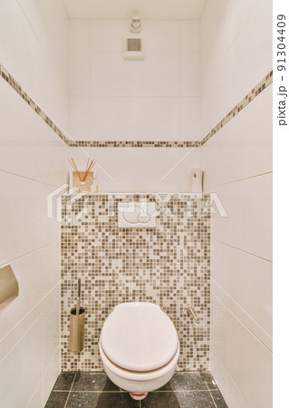 A modern toilet is installed on the wall under a button and a shelf with a diffuser in a light restroom at home A modern toilet is installed on the wall under a button and a shelf with a diffuser in a light restroom at home 91304409