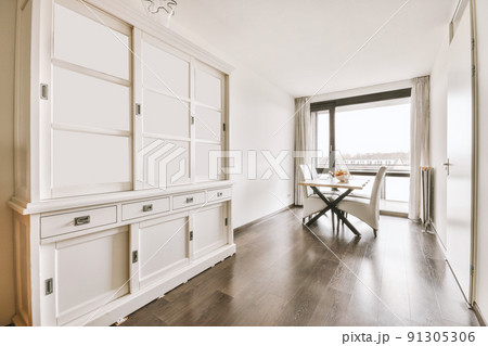 Large white wooden cupboard in the empty room with a set of chairs and dining table 91305306