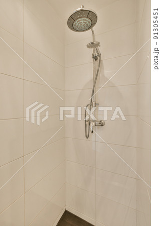 Shower faucets attached to tiled wall near glass partition and ornamental curtail in washroom at home Shower faucets attached to tiled wall near glass partition and ornamental curtail in washroom at home 91305451