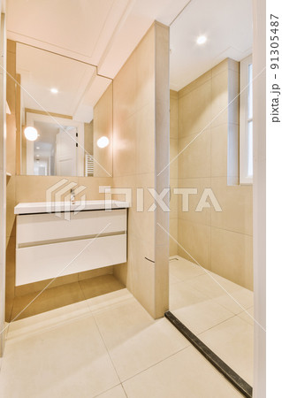 Cupboard with sink and mirror attached to tiled wall near door and drying rack in modern restroom Cupboard with sink and mirror attached to tiled wall near door and drying rack in modern restroom 91305487