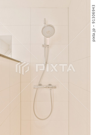 Shower faucets attached to tiled wall near glass partition and ornamental curtail in washroom at home 91306943