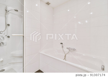 Contemporary bathroom with bathtub and glass shower cabin with light white tile and dark ceiling 91307174