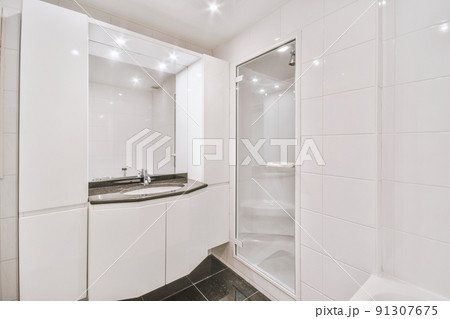 Tiled shower cabin with glass door located near sink and mirror in light restroom in contemporary apartment Tiled shower cabin with glass door located near sink and mirror in light restroom in contemporary apartment 91307675