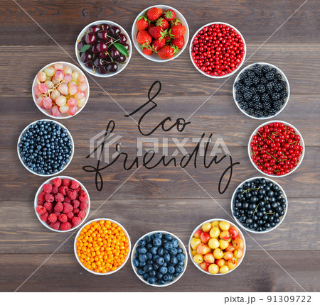 A set of berries in the round plates. Handwritten inscription - Eco friendly. Brown wooden background. Copy space. Flat top view. 91309722