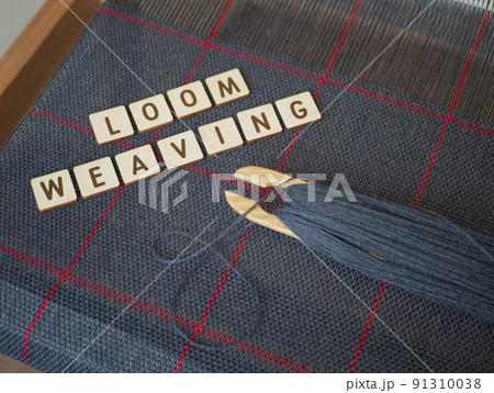 Making cloth in the traditional way. Woven blue fabric with red stripes. Concept of loom weaving, cloth art and craft. Weaving loom, wooden shuttle and handwoven scarf 91310038