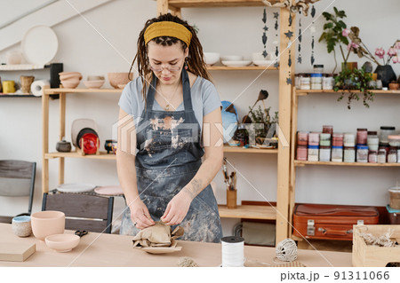 Young woman in workwear tying wrapped and packed earthenware item with thread 91311066