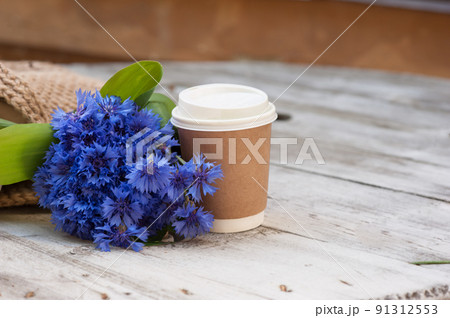 Coffee in a disposable recyclable cup with a bouquet of flowers next to it. 91312553