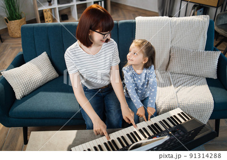 Little cute girl with music teacher having lesson at piano at school of music. 91314288