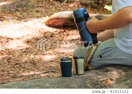 Tourist food for outdoor activities. Two metal thermo cups on a forest background. Enjoy a coffee during trips. Tourist food for outdoor activities. Two metal thermo cups on a forest background. Enjoy a coffee during trips. 91315122