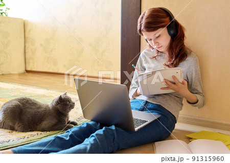 Preteen girl studying at home using laptop along with cat 91315960