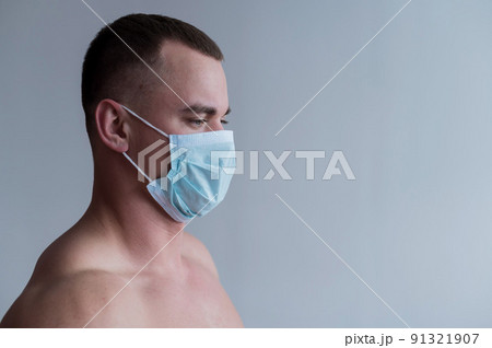 A male bodybuilder in a medical mask crossed his arms over his muscular bare chest. The guy goes in for sports in quarantine. Respiratory protection. A male bodybuilder in a medical mask crossed his arms over his muscular bare chest. The guy goes in for sports in quarantine. Respiratory protection. 91321907