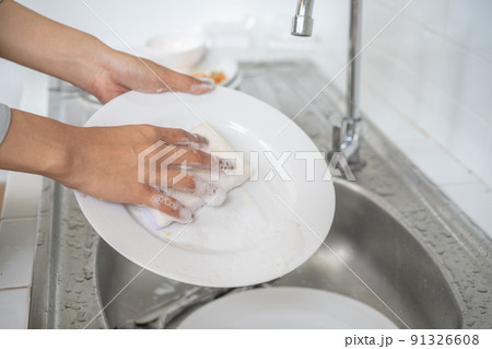Close up to Asian female washes dish in the kitchen with her dishwashing sponge. Close up to Asian female washes dish in the kitchen with her dishwashing sponge. 91326608