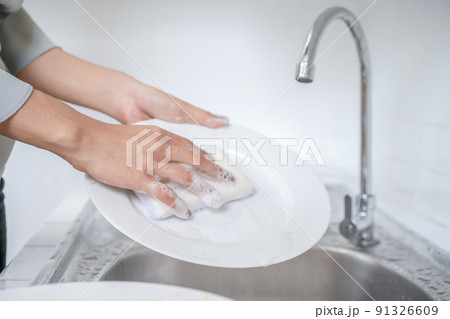 Close up to Asian female washes dish in the kitchen with her dishwashing sponge. Close up to Asian female washes dish in the kitchen with her dishwashing sponge. 91326609