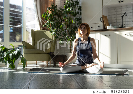 Middle aged woman practicing meditation at home, calm senior middle aged lady in lotus pose doing yoga for mental balance breathing air relaxing 91328621