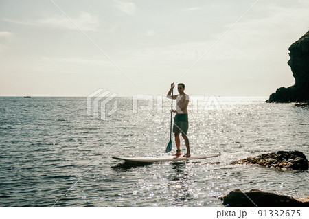 Side view foto of a man swiming and relaxing on the sup board. Sportive man in the sea on the Stand Up Paddle Board SUP. The concept of an active and healthy life in harmony with nature. 91332675