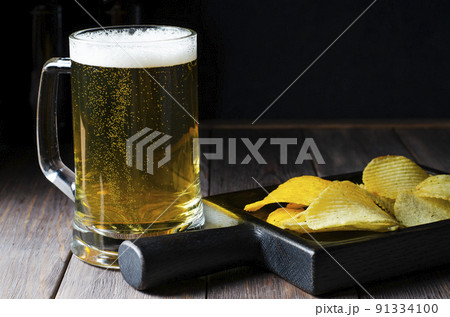 Lager beer in a glass mug. Salted potato chips. Wooden background. Copy space 91334100
