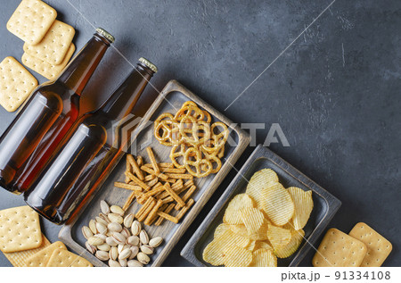 Beer in dark glass bottles and salty snacks. Dark concrete background. Top view. Free space for text. Beer in dark glass bottles and salty snacks. Dark concrete background. Top view. Free space for text. 91334108