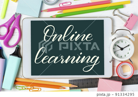 Online learning - handwritten inscription on a tablet. The concept of distance training for children. Tablet and office supplies on a white wooden background. 91334295