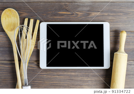 A tablet computer and cooking battery on a brown wooden background. Copy space. Concept of cooking recipes A tablet computer and cooking battery on a brown wooden background. Copy space. Concept of cooking recipes 91334722