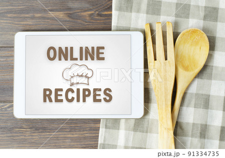 Online recipes. Cookbook in a tablet computer. Kitchen utensils. Brown wooden background Online recipes. Cookbook in a tablet computer. Kitchen utensils. Brown wooden background 91334735