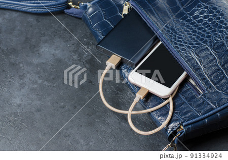 Blue Power Bank and telephone in the women's bag. Dark grey concrete background. Copy space Blue Power Bank and telephone in the women's bag. Dark grey concrete background. Copy space 91334924