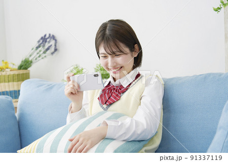 リビングのソファーの上ででスマホを見る女子高生 91337119