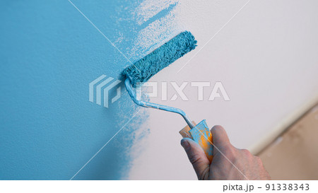 Hand holds roller and paints wall blue closeup 91338343