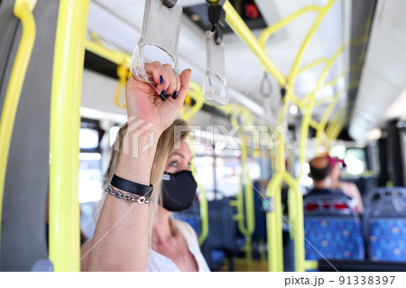 Hand of tourist passenger in protective mask holding handrails in bus 91338397
