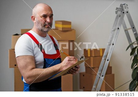 Middle-aged man mover in uniform making notes on clipboard 91338515