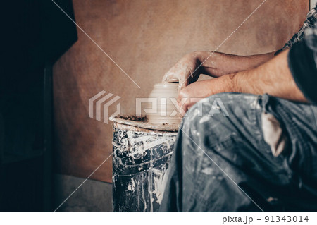 Man forms clay jar on potter's wheel. Potter in the process of work side view 91343014